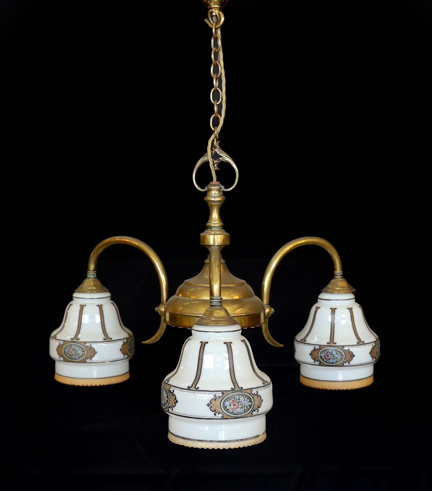 An early 20th century English lacquered brass light fitting with three stencilled opaque glass shades, height 65cm. width 50cm